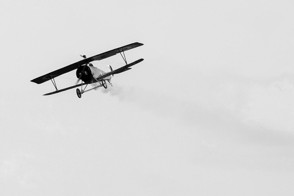 Black and white photo of a WWI biplane flying toward the camera trailing smoke