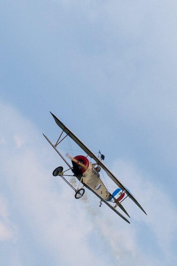 Nieuport biplane banking steeply downward against a pale blue sky