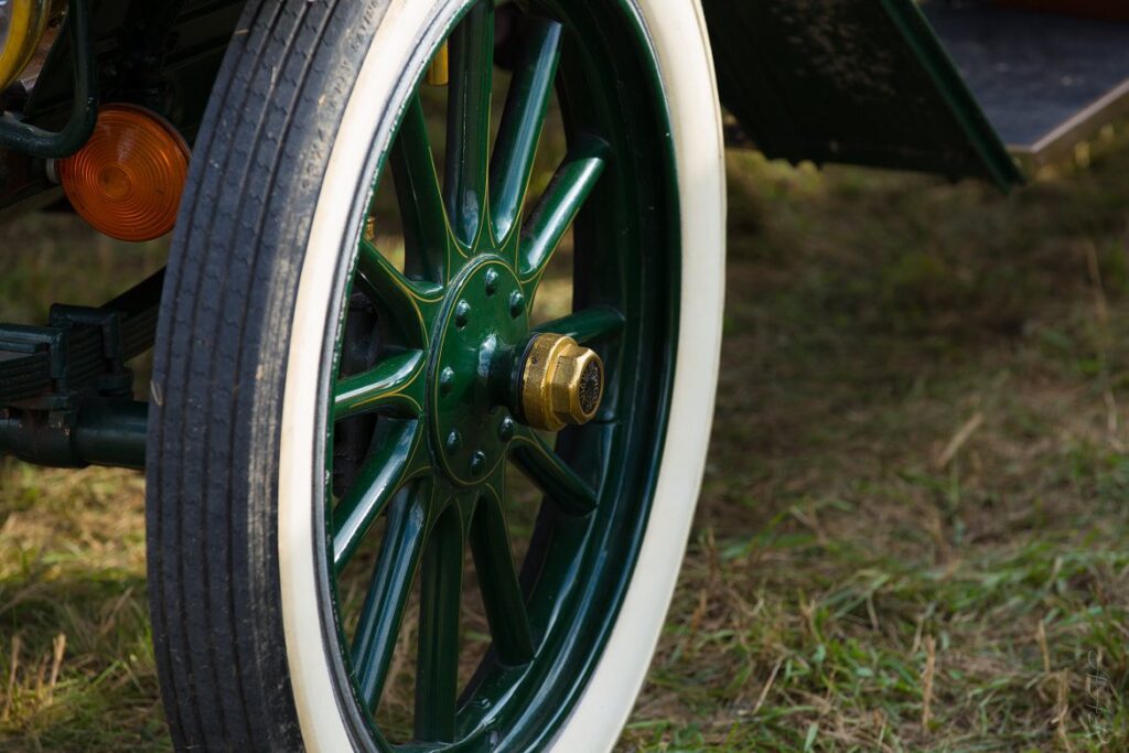 Close-up of a green-spoked wheel with a brass hub cap and a white tire on an antique car