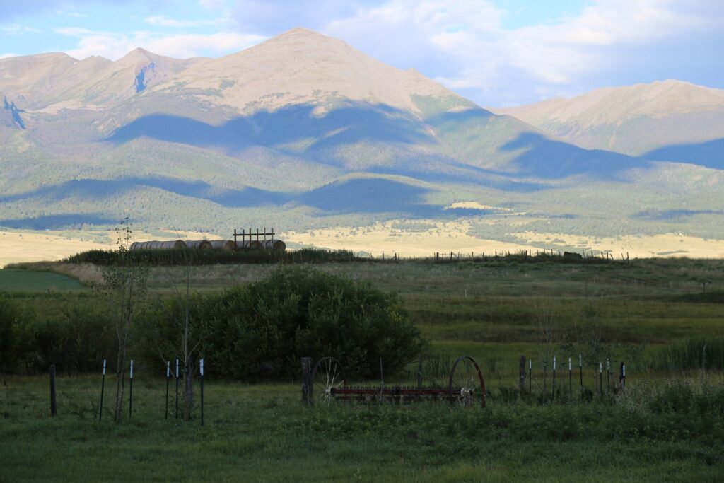 Green valley pasture with an old fence and farm equipment below a big range of mountains