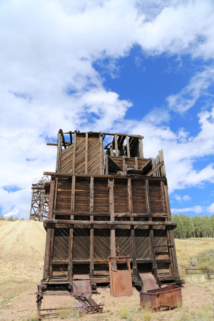 Tall weathered wooden mine headframe and ore house under a blue sky with clouds