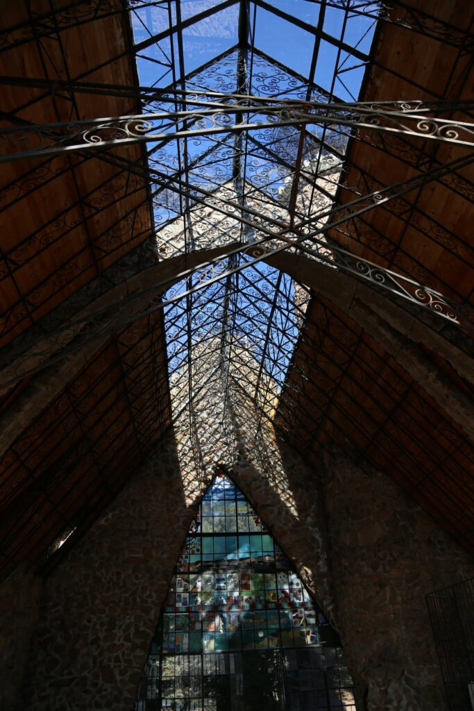 Looking up at an iron and glass peaked roof with a tall stained glass window below