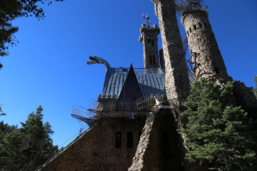 Stone castle towers and a metal dragon head sticking out from the roof against a deep blue sky