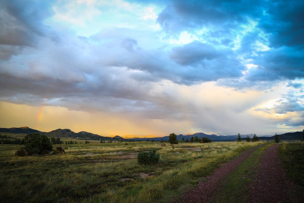 Dramatic storm clouds and a hint of rainbow over a valley with a dirt road