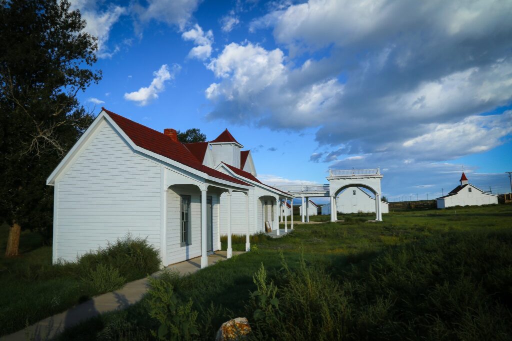 White ranch buildings with red roofs and an arched gateway under a blue sky with clouds