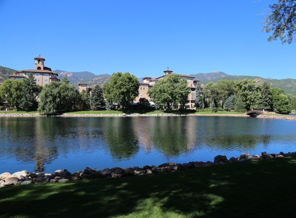 Pink stucco hotel towers across a calm blue lake with mountains behind