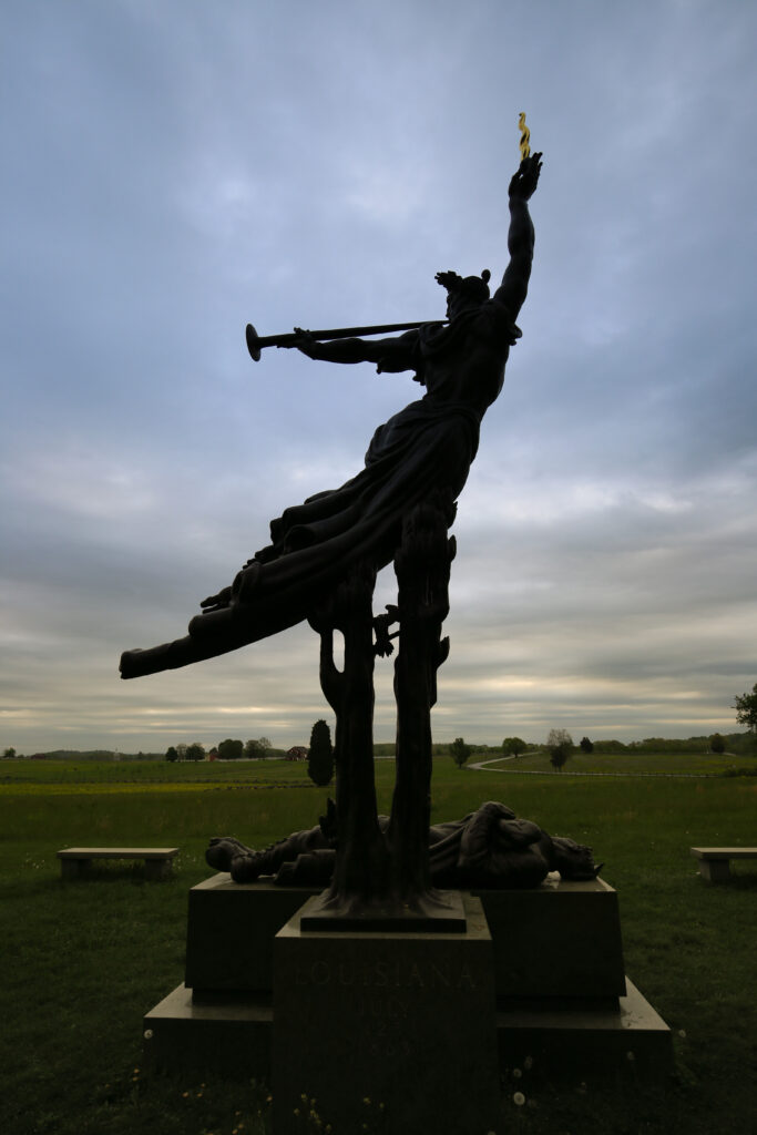 Silhouette of a bronze figure blowing a trumpet and holding up a flaming cannonball over a fallen soldier, Louisiana State Memorial