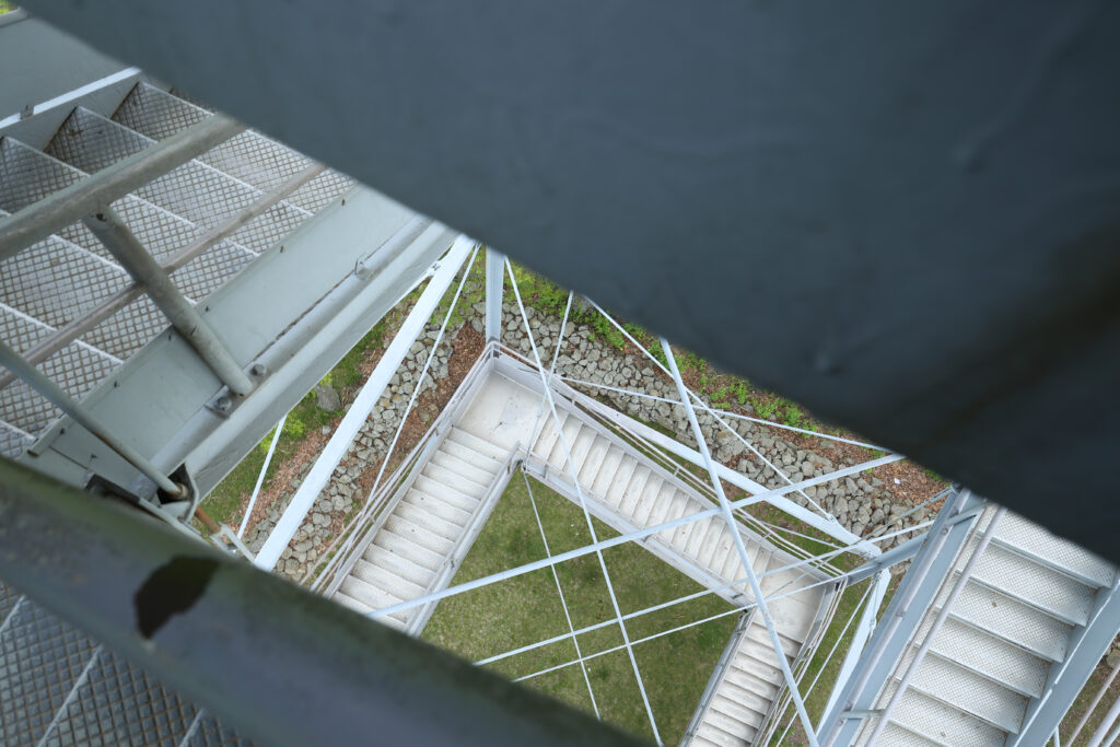 Looking straight down the zigzagging steel staircase of an observation tower to the grass far below