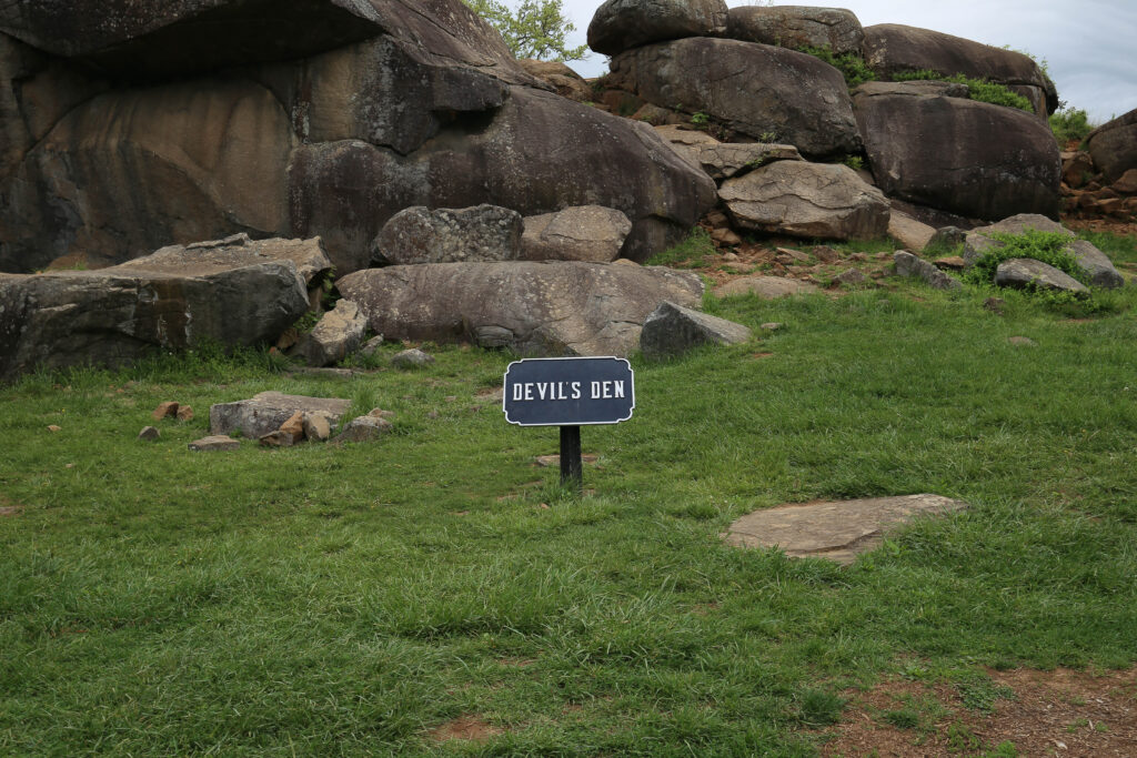 Huge boulders of Devil's Den piled on a grassy slope, with a small sign reading Devils Den