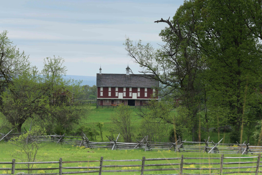 Red barn with two white cupolas seen between spring trees, behind a split-rail fence and a board fence