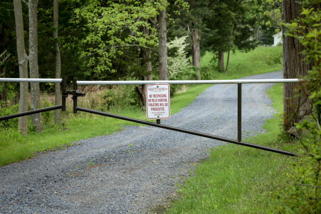 Metal gate across a gravel lane in the woods with a sign reading no trespassing or relic hunting, violators will be prosecuted