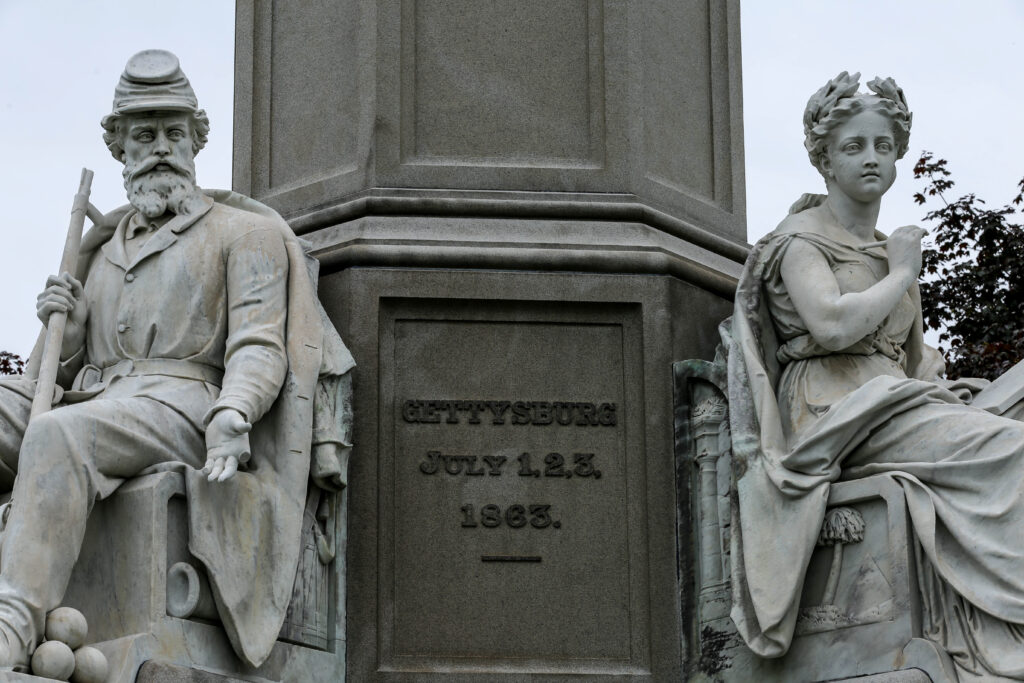 Marble figures of a bearded Union soldier and a laurel-crowned woman at the base of the Soldiers' National Monument, inscribed Gettysburg July 1, 2, 3, 1863