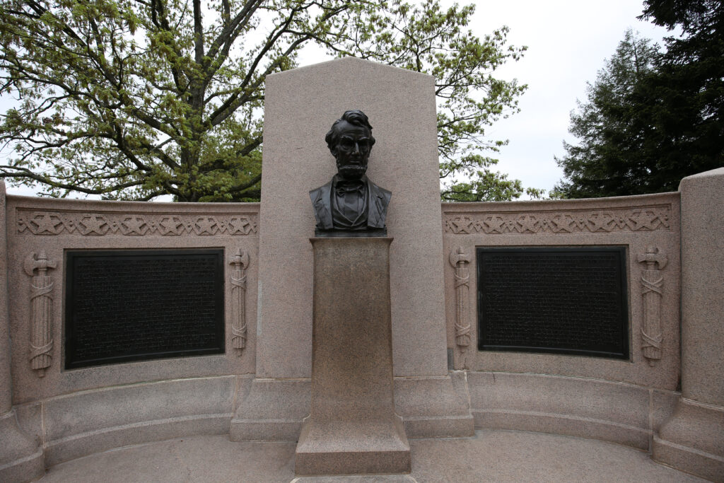 Bronze bust of Abraham Lincoln on a granite pedestal between two bronze tablets in a curved granite memorial
