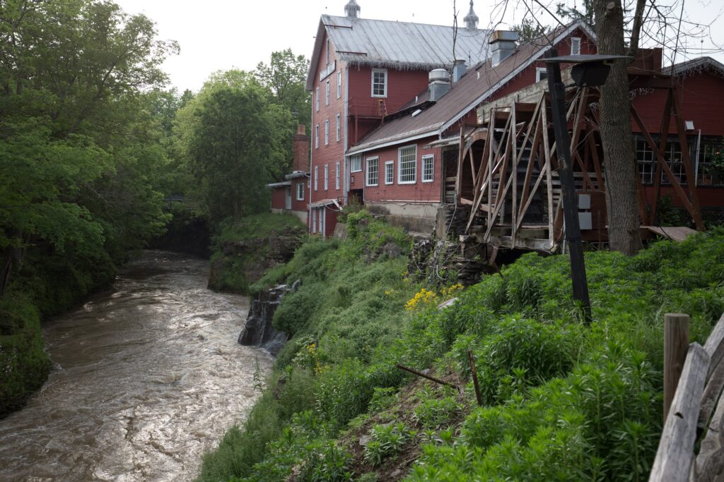 Clifton Mill's red buildings and water wheel on a grassy bank above the rushing Little Miami River