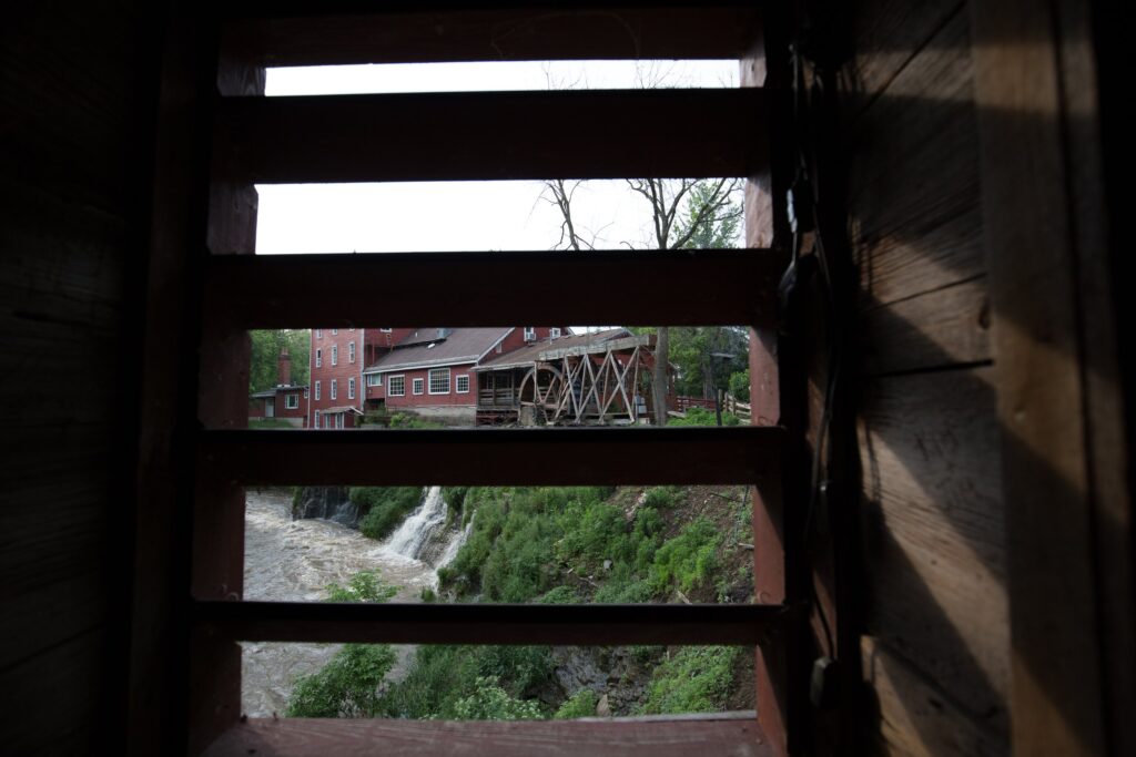 Clifton Mill and a waterfall framed between the open treads of a dark wooden staircase