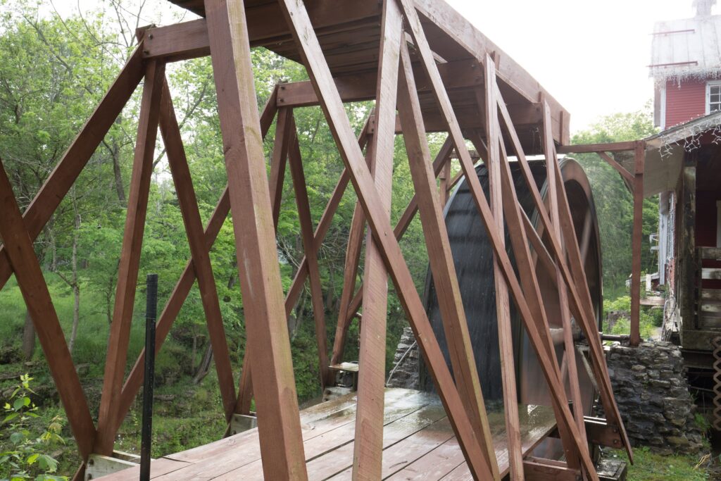 Heavy wooden truss framing in the foreground with Clifton Mill's large water wheel behind it among green trees