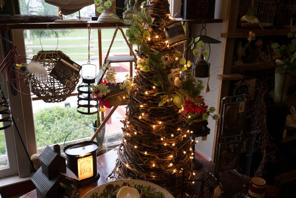 Cone-shaped grapevine tree wrapped in warm string lights inside the shop, with baskets and lanterns by a window
