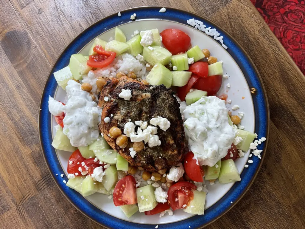 Acropolis Bowl on a blue-rimmed plate: grilled chicken with dill and feta over rice, with crispy chickpeas, cucumber, tomatoes and tzatziki