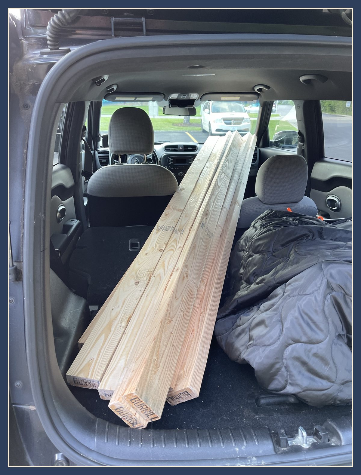 A bundle of eight-foot 2x4s loaded through the back hatch of a Kia, reaching up between the front seats.