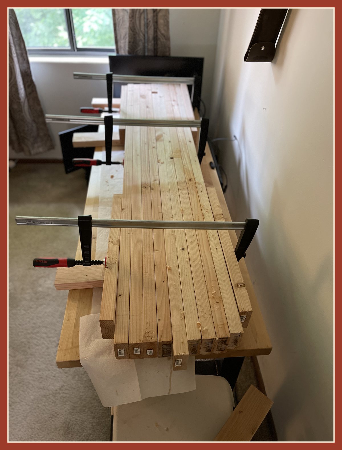 The glued-up slab of 2x4s clamped tight with long bar clamps, drying indoors.