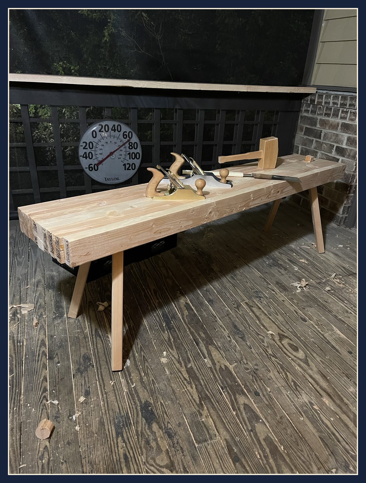 The finished low Roman workbench on the porch at night, with two hand planes and a mallet on top.