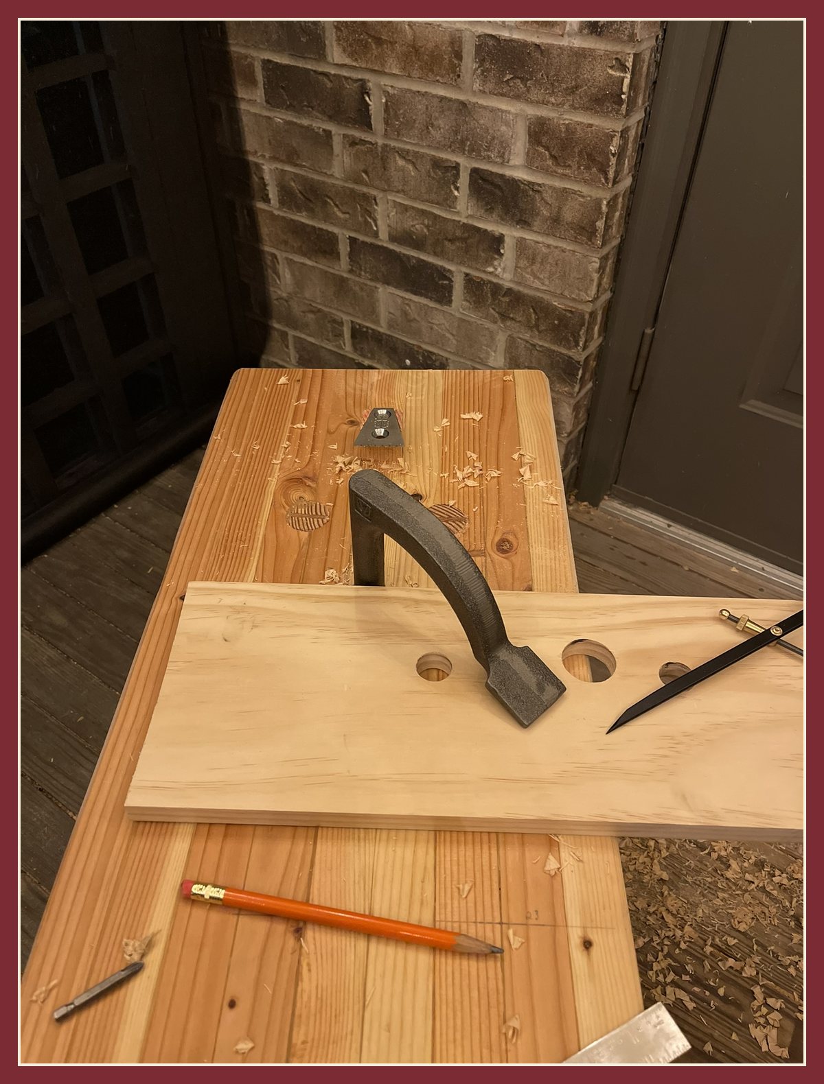 A holdfast pinning a board to the bench top, with a pencil nearby.