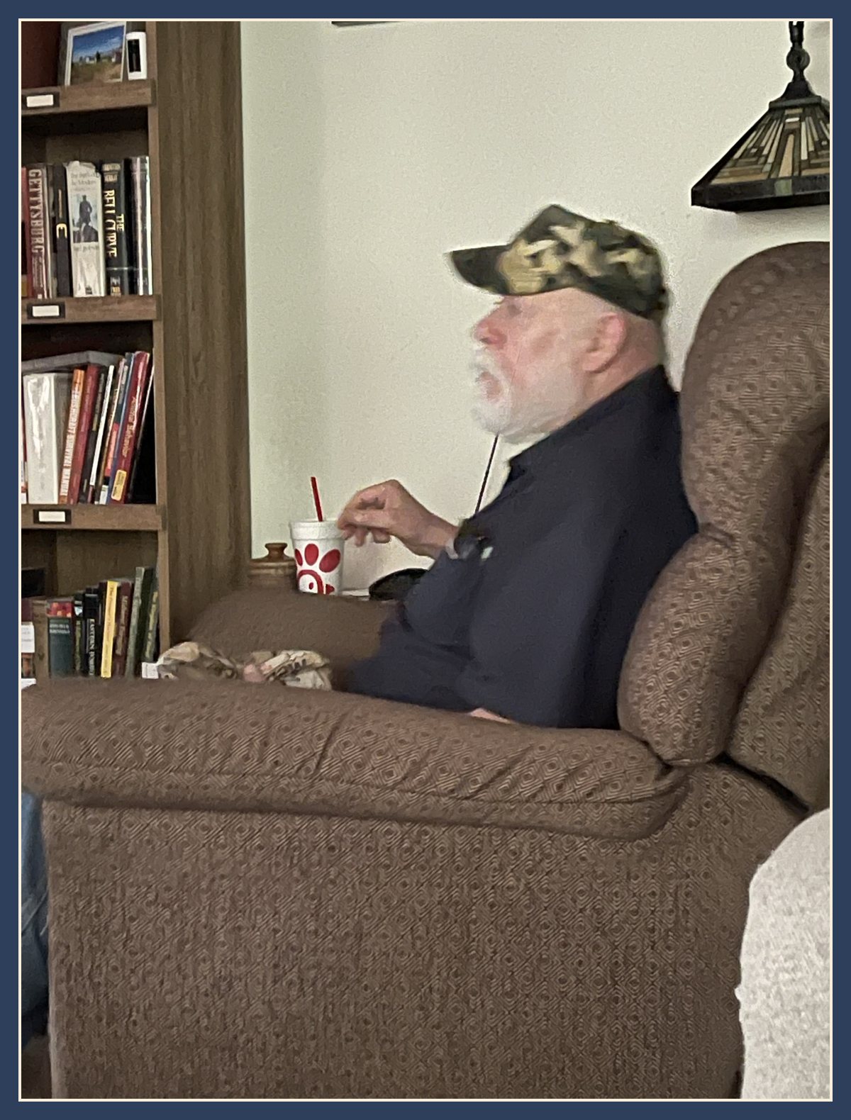 Adam's dad in a camo cap, sitting in a recliner with a drink, on the day the bench got its linseed oil.