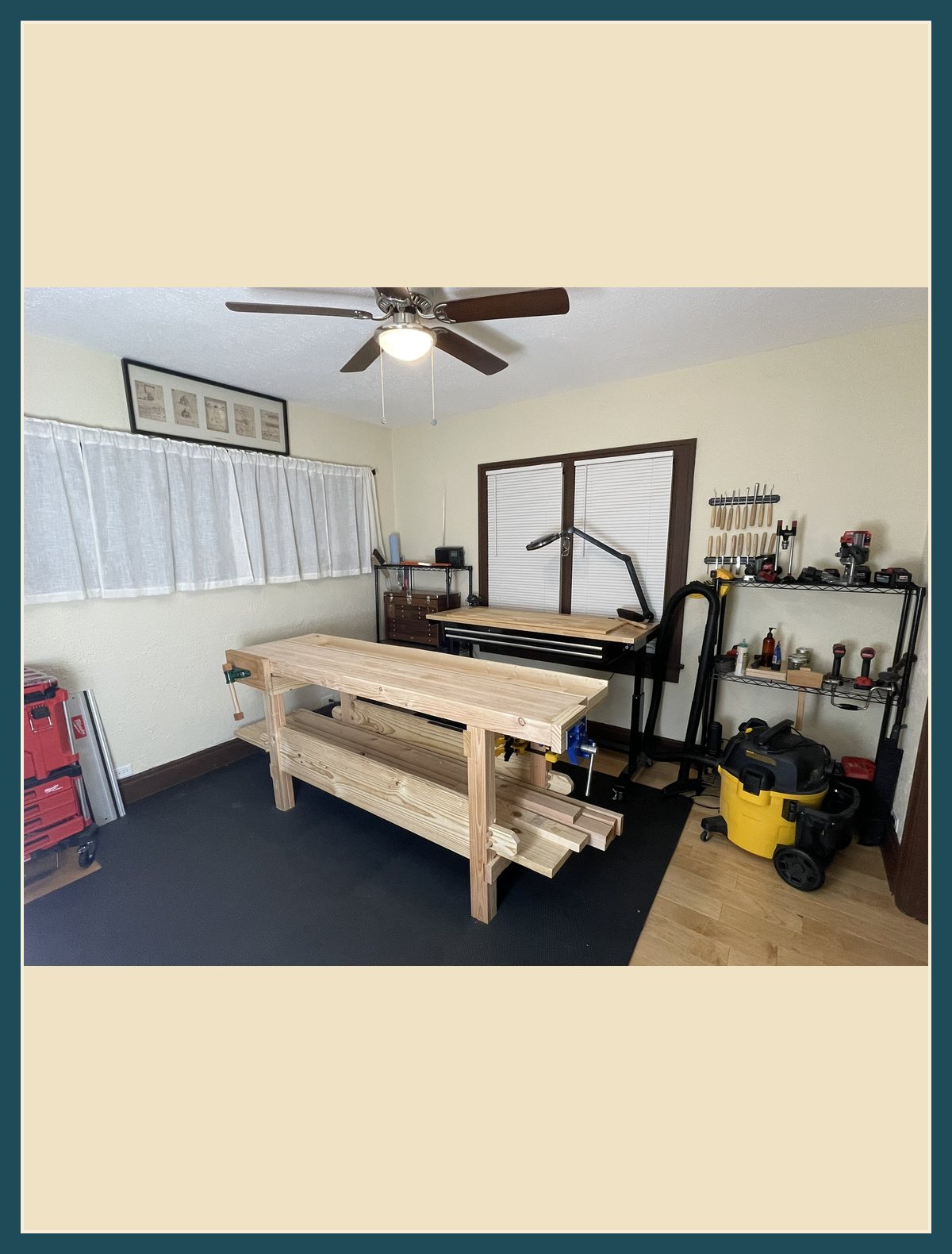 Adam's current workbench, a full-height bench with lumber stacked on the shelf underneath, in his shop.