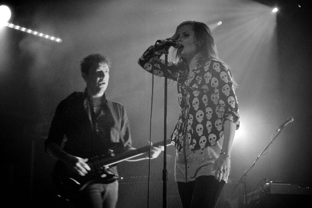Black-and-white photo of The Kills on stage, the singer at the mic and the guitarist beside her